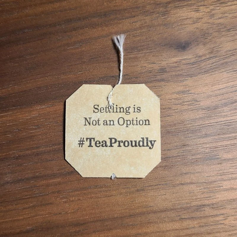 A tea-bag tag on a wooden desk that reads: Settling is Not an Option.